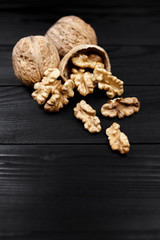 Walnut and walnut kernels and whole walnuts on rustic black wooden background.