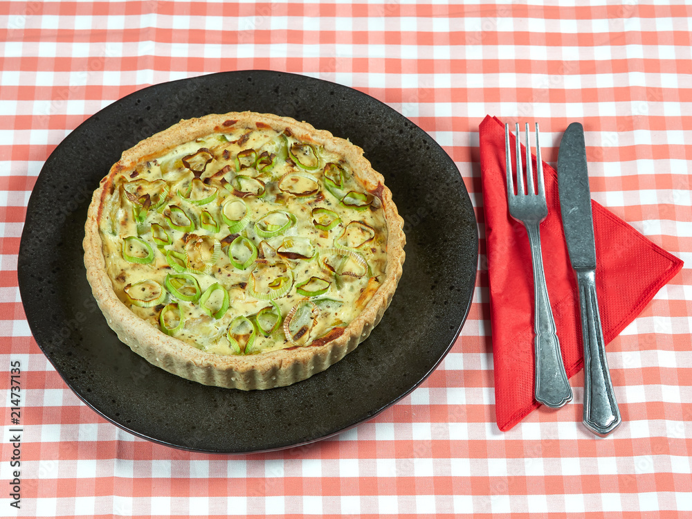 Wall mural homemade zucchini, leek and ricotta quiche set on a dark plate, on a red table cloth, with a fork an