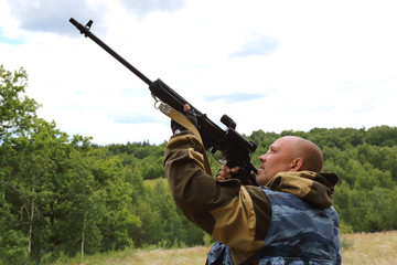 Hunting season. Male 35-40 years old, a hunter is aiming at the sky from a firearm in the forest.