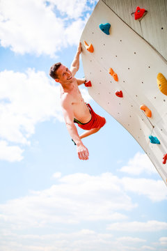 Photo of smiling athlete looking at camera practicing on wall for rock climbing against blue sky with clouds