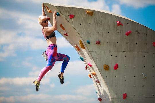 Photo from side of sports girl in leggings hanging on wall for climbing against blue sky