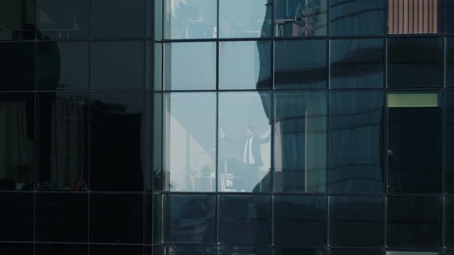 Aerial View Footage: From Outside into Office Building with Businessman Working and Looking out of the Window. Beautiful Flying Away Shot of The Financial Business District Skyscrapers. 