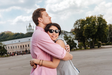 Sincere love. Satisfied dreamful couple exchanging hug and posing on blurred background