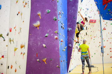Photo of young sports girl exercising on climbing wall with trainer