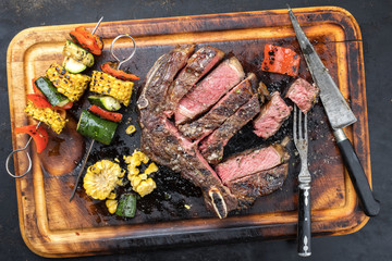 Barbecue dry aged wagyu cutlet with vegetable skewer as top view on a burnt cutting board
