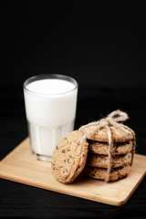 Tasty cookies and glass of milk on rustic black wooden background.