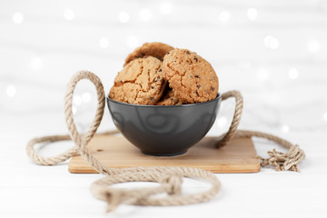 Delicious chocolate cookies in a dish on the wood white background decorated with a rope.