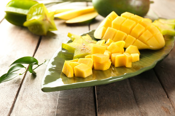 Plate with pieces of fresh mango and starfruit on wooden table