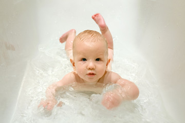 Очаровательный ребенок купается в ванной. Лежит на животе. - obrazy, fototapety, plakaty
