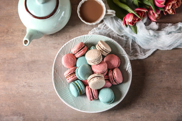 Plate with tasty macarons and coffee set on table, top view