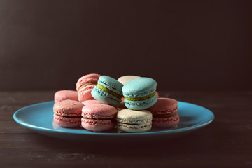 Plate with tasty macarons on table against dark background