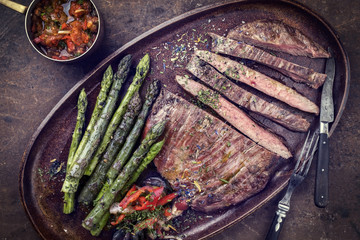 Barbecue dry aged wagyu flank steak with green asparagus and chili relish as top view on a plate