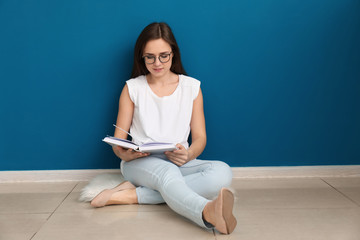 Young woman reading book on floor near color wall