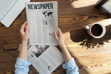 Naklejka premium Young woman reading newspaper at table