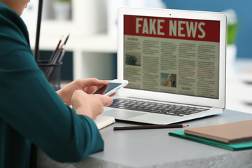 Woman with phone reading news on laptop indoors