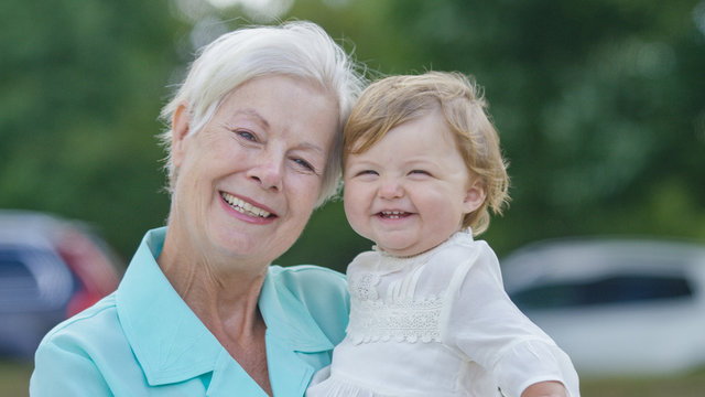 Grandmother Holding Her Grandchild And Smiling To Camera 