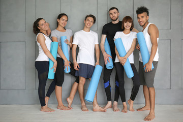 Fototapeta premium Group of sporty people with yoga mats near grey wall