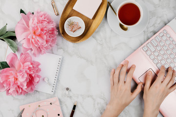 Feminine flatlay mockup with pink peonies, daisies, notebooks, cup of warm tea and female hands...