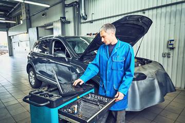 mechanic man with automotive diagnostic scanner and clipboard checking car system at workshop