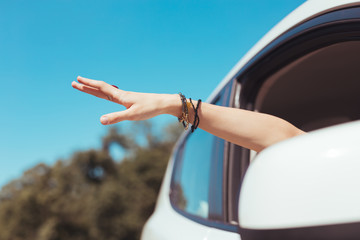 Hand out. Woman taking her hand with many stylish bracelets out of car window while traveling with...