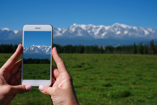 Woman's hand is holding smartphone and take a photo of mountains.