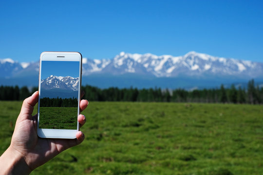 Woman's hand is holding smartphone and take a photo of mountains.