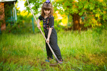 Happy little girl help parents in garden with rake. Seasonal garden work. Backyard cleaning