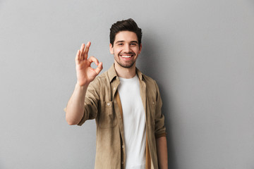 Portrait of a happy young casual man showing ok gesture - obrazy, fototapety, plakaty