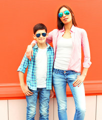 Fashion mother with son teenager in a sunglasses, checkered shirts on orange background