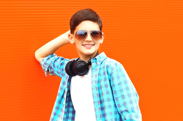 Happy smiling child boy in a sunglasses and wireless headphones on a colorful orange background