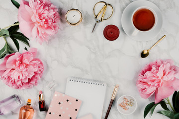Feminine flatlay mockup with pink peonies, daisies, notebooks, cup of warm tea, cosmetics and stationery on marble table