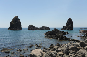 View on the rocky islands in Aci Trezza, Sicily, Italy, with the Islands of the Cyclops in the background.