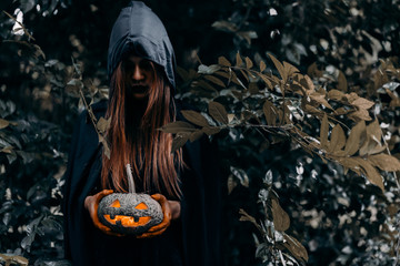 Witch holding pumpkin carved halloween horror concept, psychopomp evil wicked at dark forest with copy space the right.