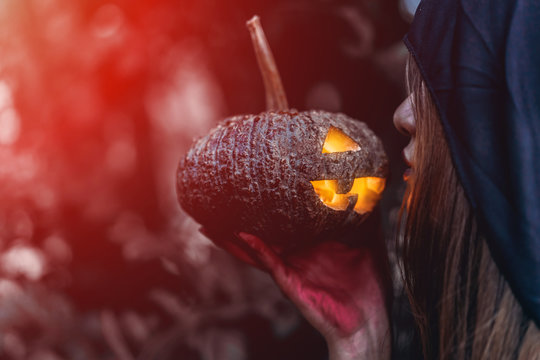 Witch Kissing pumpkin carved halloween horror concept, psychopomp evil wicked costume at dark forest with copy space the left.