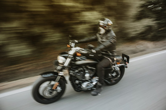 Blurry motion image of man riding a black American motorcycle on the road.