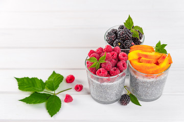 Food and drink, healthy eating and dieting concept. Homemade white chia pudding with fresh berries and green leaves for breakfast on a light kitchen table. Three glasses, raspberry, blackberry,apricot