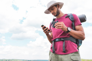 male traveler with backpack and binoculars using smartphone