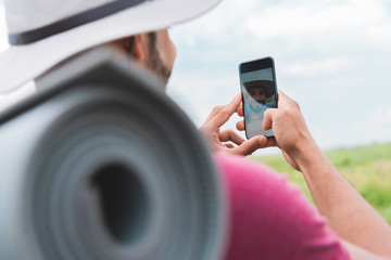 hiker with backpack and tourist mat taking selfie on smartphone