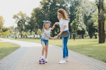 Active walk. Pleasant stylish preschool girl wearing jeans shorts and white and blue shirt having active walk with her mother