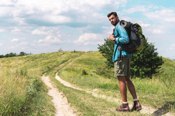 Fototapeta na wymiar handsome hiker with backpack walking on green meadow