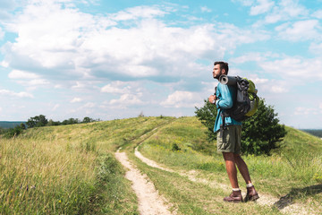 Obraz premium handsome traveler with backpack walking on green meadow with beautiful sky