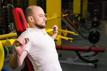 Sport, fitness, training and people concept - Man doing heavy exercise pumping up muscles in gym