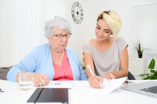 Young Woman Helping Old Senior Woman Doing Paperwork And Administrative Procedures With Laptop Computer At Home