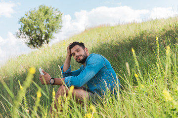 Naklejka na ściany i meble male traveler using smartphone on green summer meadow with tree