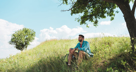 handsome traveler with backpack sitting on green summer meadow