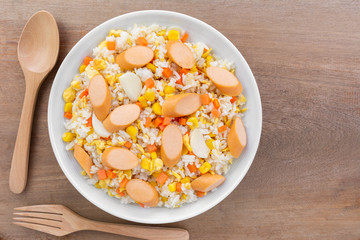 top view of fried rice with sausage and vegetable in a ceramic dish on wooden table. homemade style food concept.