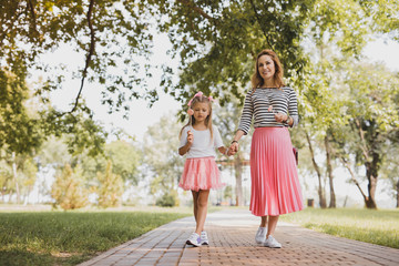 Walking with mother. Cute beautiful girl wearing short pink skirt with lollipop in her hand walking with mother