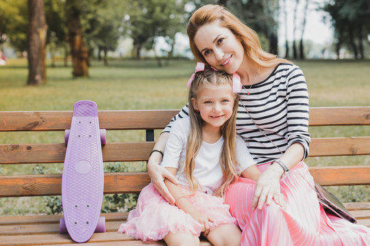 Sitting on bench. Blonde-haired mother and daughter feeling relaxed while sitting on bench in the park