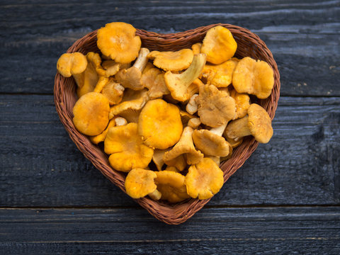 Orange chanterelle mushrooms lie in a wooden basket in the shape of a heart on a black background