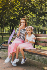 Fashionable sneakers. Stylish mother and daughter wearing fashionable sneakers while sitting on bench in the park